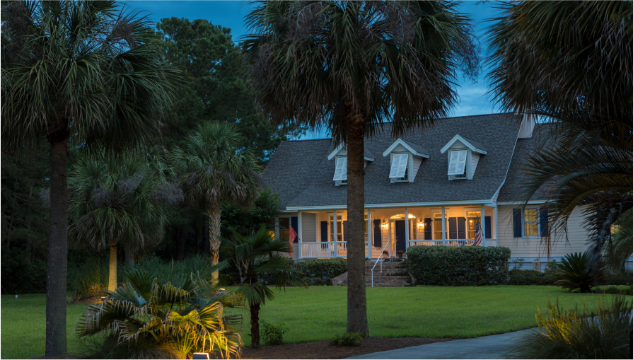 Beautiful cape cod house lit up at twilight with palm trees